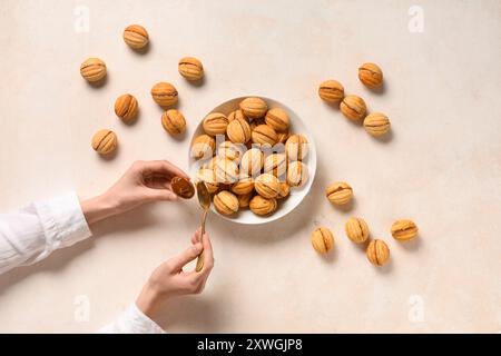 Donna che prepara gustosi biscotti a forma di noce con latte condensato bollito su un tavolo grunge bianco Foto Stock