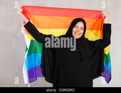 Felice giovane donna vestita con abiti tradizionali islamici con bandiera arcobaleno Foto Stock