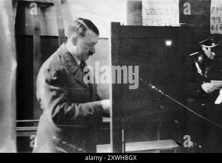 Adolf Hitler vota in una tribuna elettorale a Berlino. La data della foto è il 1933, il che significa che è stata scattata durante le elezioni generali organizzate dopo che Hitler è stato messo al potere. Per queste elezioni Hitler aveva arrestato tutti i deputati del partito comunista, distrutto gli uffici del partito comunista e reso illegale il partito. Senza un'opposizione efficace e un atteggiamento positivo nel paese, i nazisti vinsero queste elezioni (l'unica che fecero), che aprirono la porta alla legge sull'abilitazione e a tutte le catastrofi successive. Foto Stock