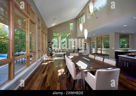 Moderna sala da pranzo e soggiorno con molte finestre su più livelli che si affacciano su alberi verdi e patio Foto Stock