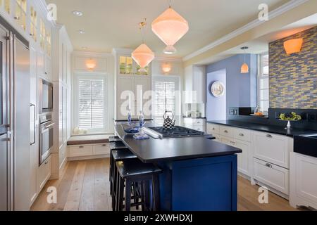 Splendida cucina di lusso con armadi bianchi, pareti blu e ripiani neri Foto Stock