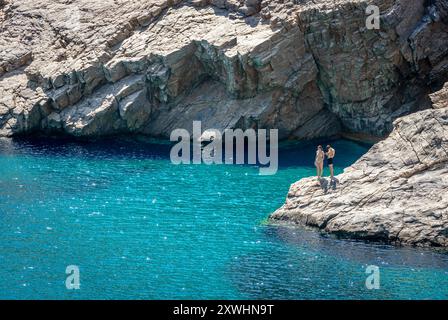 Una giovane coppia si erge sulle scogliere all'estremità della spiaggia di Mouros, un'incredibile spiaggia di ciottoli nell'isola di Amorgos, Cicladi, Grecia. Foto Stock