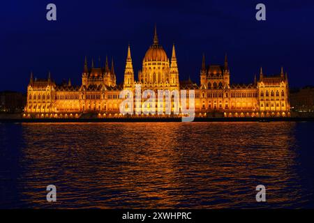 Splendida vista notturna che mostra l'edificio del Parlamento ungherese illuminato che si riflette sull'acqua del fiume, mettendo in risalto la bellezza architettonica e la vibrante città Foto Stock