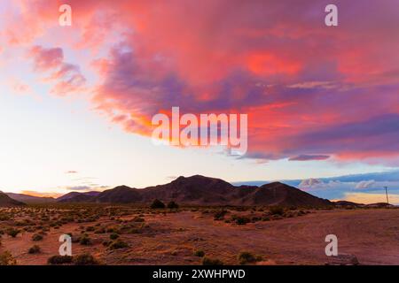 Maestose nuvole dipinte in vibranti sfumature di rosa e viola gradiscono il cielo mentre il sole tramonta dietro le montagne. Un momento pittoresco per catturare Califo Foto Stock