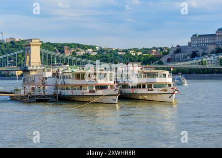 Budapest, Ungheria - 7 luglio 2024: Vista panoramica delle barche turistiche attraccate sul Danubio, con il Ponte delle catene di Budapest e il Castello di Buda nel retro Foto Stock