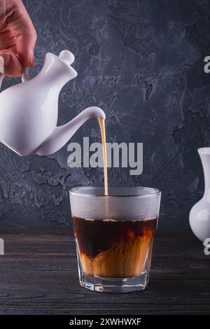 Versare una crema ricca e vellutata in un rinfrescante bicchiere di caffè Cold Brew per un perfetto sorso mattutino Foto Stock