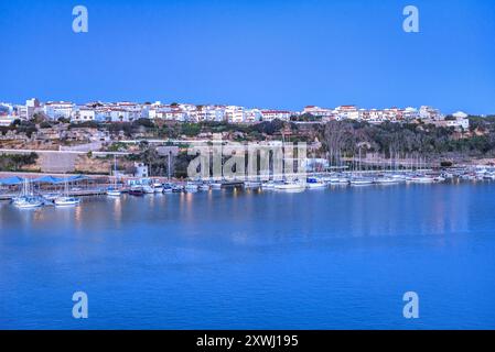 Città di Maó / Mahón, di notte e nell'ora blu, prima che sorga il sole, vista da un traghetto nel porto di Maó (Minorca, Isole Baleari, Spagna) Foto Stock