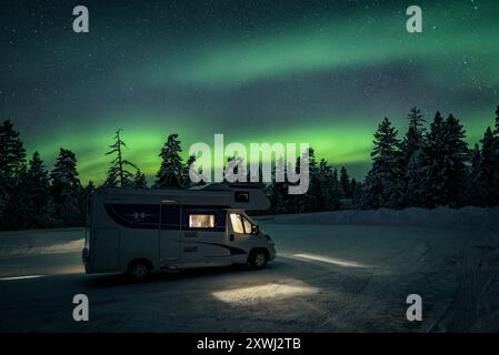 Aurora boreale su un camper e una foresta innevata di notte (Lapponia, Finlandia). Es: Aurora boreale sobre una autocaravana y un bosque nevado, Laponia Foto Stock