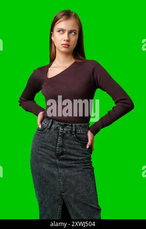 Giovane donna con maglione marrone e jeans che posa contro schermo verde Foto Stock