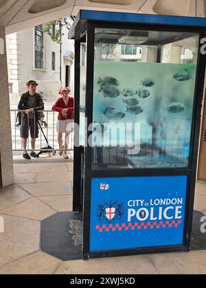 Londra, Regno Unito. 14 agosto 2024. La scatola di sentinelle della polizia con l'opera d'arte di Banksy raffigurante i piranha, che si trovava originariamente su Ludgate Hill, è stata ora spostata a Guildhall da funzionari della City of London. Due donne che scattano selfie sul cellulare. Foto Stock