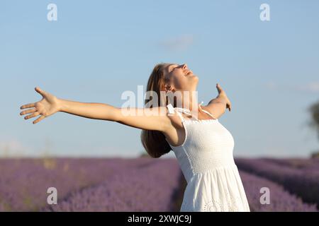 Donna eccitata che indossa un abito bianco che celebra una giornata di sole nel campo della lavanda Foto Stock