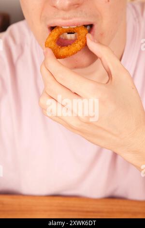 Un uomo caucasico mangia con le mani anelli di cipolla fritti freschi, cultura fast food americana Foto Stock