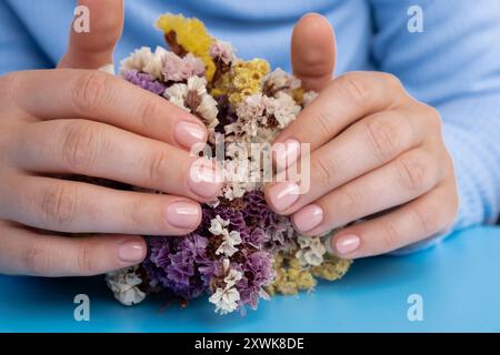 Unghie pastello morbide e curate su sfondo blu. Donna che mostra la sua nuova manicure nei colori della tavolozza pastello. Decorazioni semplici, fresche vibrazioni primaverili dai colori naturali Foto Stock