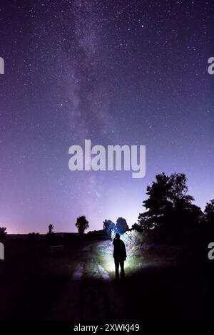 Una persona che cammina nella campagna di notte con una torcia frontale sotto le stelle della via Lattea Foto Stock