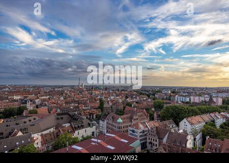 Nürnberger Stadtbild am Abend Luftaufnahme der Nürnberger Altstadt von einem erhöhten Standpunkt. Die Dächer der historischen Gebäude erstrecken sich weit bis zum Horizont, wo Industrieanlagen und moderne Gebäude das Stadtbild ergänzen. Der Himmel zeigt eine beeindruckende Wolkenformation, während die untergehende Sonne das Panorama in warmes Licht taucht. Nürnberg Bayern Deutschland *** paesaggio urbano di Norimberga di sera Vista aerea del centro storico di Norimberga da una posizione elevata i tetti degli edifici storici si estendono fino all'orizzonte, dove si alternano impianti industriali e edifici moderni Foto Stock