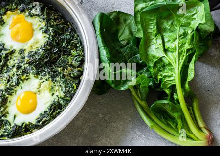 Spinaci arrostiti e uova fritte in stufato con verdure fresche di spinaci su tavola rustica Foto Stock