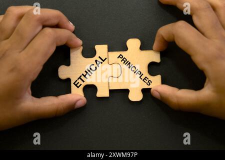 Due mani collegano pezzi di puzzle etichettati "etici" e "principi", che simboleggiano l'integrità e il processo decisionale morale. Foto Stock