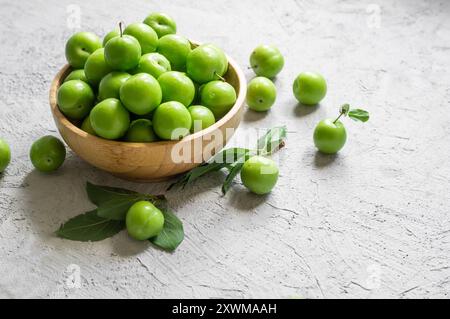 Prugne verdi biologiche mature fresche o greEngage in ciotola su fondo rustico bianco, concetto di abbondanza di frutta estiva Foto Stock