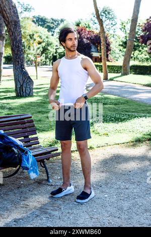 Un uomo con canotta bianca e pantaloncini neri si trova in un parco Foto Stock