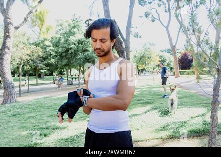Un uomo con canotta bianca e pantaloncini neri indossa un cinturino da polso blu Foto Stock