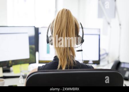 Eine Frau traegt Kopfhoerer in einem Buero a Berlino, 08.08.2024. Arbeit in einem Callcenter Berlin Deutschland *** Una donna indossa le cuffie in un off Foto Stock