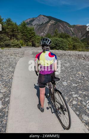 Ciclista donna su una pista attraverso un letto di fiume essiccato nelle Alpi francesi vicino a Bourg d'Oisans. Foto Stock