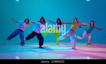 Espressione di sé attraverso la danza dinamica. Ragazze giovani, adolescenti che si esibiscono hip hop sul palco su sfondo blu ciano su sfondo neon Foto Stock