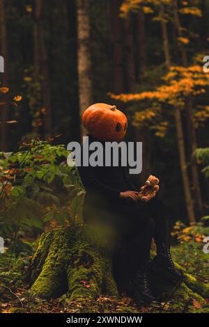 donna spaventosa con testa di zucca nella foresta con giocattolo Foto Stock