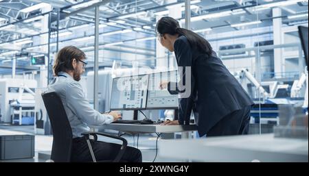 Bell'ingegnere e un bellissimo International Business Manager che parla e usa il computer desktop. Specialisti che impostano valori di produzione in un impianto di assemblaggio elettronico Foto Stock