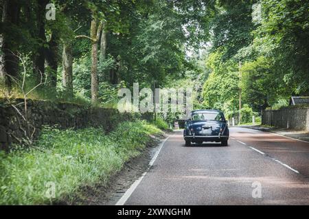 Un'auto d'epoca passa davanti a pittoreschi cottage su una strada tranquilla nella pittoresca campagna scozzese Foto Stock