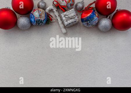 Disposizione piatta di ornamenti natalizi rossi e argentati su sfondo bianco testurizzato, perfetta per le feste o per biglietti d'auguri con spazio per il testo Foto Stock