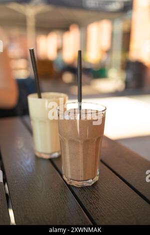 Due cocktail di latte di frutta rosa in bicchieri con tubetti neri a spirale per frullati, cocktail e succhi di frutta in piedi sul tavolo nel caffè di strada. Bokeh Foto Stock