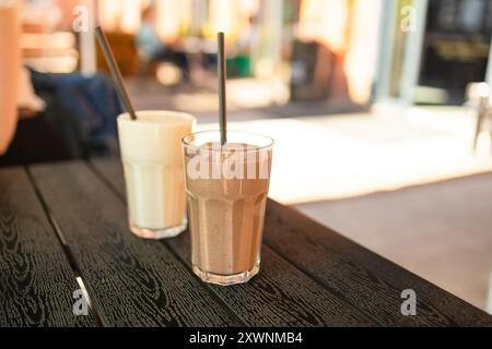 Due cocktail di latte di frutta rosa in bicchieri con tubetti neri a spirale per frullati, cocktail e succhi di frutta in piedi sul tavolo nel caffè di strada. Bokeh Foto Stock