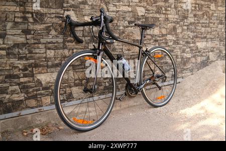 Bicicletta da corsa appoggiata contro un muro di pietra. Bici da strada parcheggiata sul marciapiede. Concetto di ciclismo urbano e trasporto ecologico Foto Stock