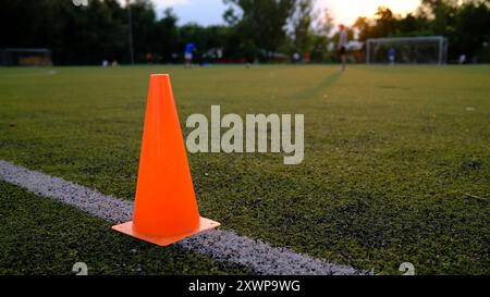 Cono da allenamento arancione sul campo di calcio al tramonto. Attrezzatura da calcio su erba con gol sullo sfondo. Concetto di allenamento sportivo Foto Stock