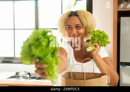 Striscione con una giovane donna afroamericana in piedi in cucina che tiene la lattuga Foto Stock