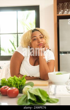 Donna afroamericana curvy con un volto triste che guarda a tavola con verdure. Foto Stock