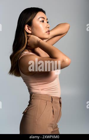 Una giovane donna, vestita con canotta rosa e pantaloni marroni, guarda in lontananza. Foto Stock