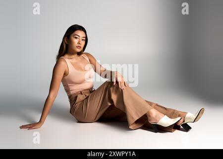 Giovane donna seduta in posa rilassata, outfit elegante impreziosito dal suo sguardo. Foto Stock