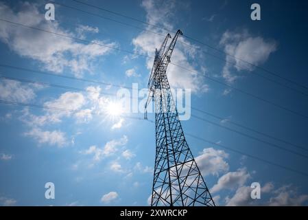 un pilone ad alta tensione, vista senza fine, retroilluminato con sole, cielo blu e nuvole bianche Foto Stock