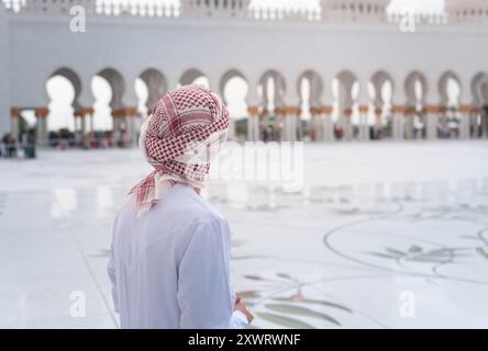 Un uomo arabo in kandora si trova nella grande moschea dello sceicco Zayed nel cortile di Abu Dhabi, che presenta un'impressionante architettura islamica con un'intricata cupola Foto Stock