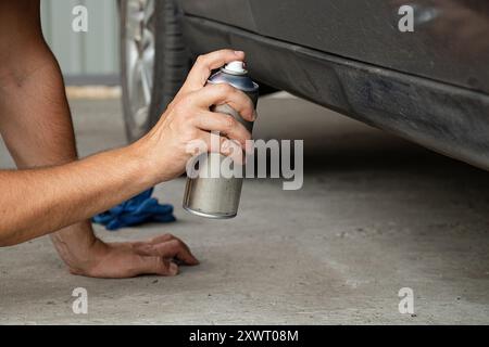 Un uomo spray dipinge un'auto in un cortile con vernice nera, nascondendo la ruggine sull'auto Foto Stock