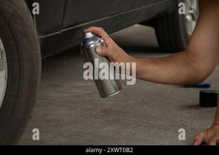 Un uomo spray dipinge un'auto in un cortile con vernice nera, nascondendo la ruggine sull'auto Foto Stock