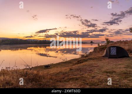 Le avventure di pesca, la pesca alla carpa. Il pescatore, al tramonto, è la pesca con carp fishing tecnica. Campeggio in riva al lago. Foto Stock