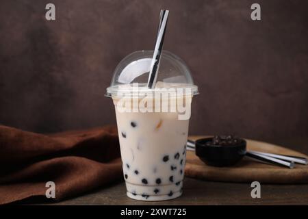 Gustoso tè con bolle di latte in una tazza di plastica su un tavolo di legno su sfondo marrone Foto Stock