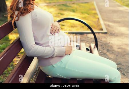 Giovane donna incinta felice seduta sulla panchina nel parco estivo Foto Stock