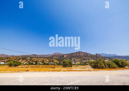 Splendida vista del paesaggio costiero montano lungo il Mar Mediterraneo, con strada sterrata e ville annidate alla base delle montagne di Creta. Foto Stock