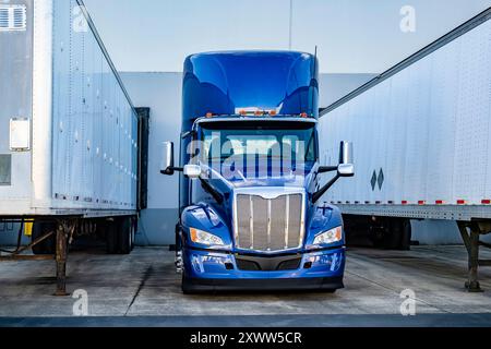 Trattore industriale Shine Blue potente semi-motrice con carro di grandi dimensioni con cabina corta e spoiler per tetto in piedi tra due semirimorchi frigoriferi di carico Foto Stock