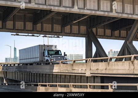 Semi-autocarro di grandi dimensioni con Day Cab bianca per il trasporto di carichi commerciali in un semi-rimorchio a basso profilo per furgoni asciutti che si trovano all'intersezione stradale del cavalcavia lungo il Foto Stock