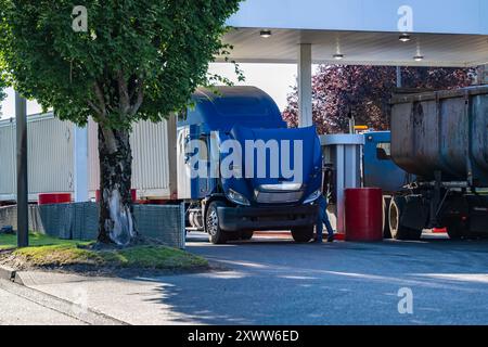 Semi-motrice da carro di perforazione blu di livello industriale con cofano aperto e semirimorchio per container parcheggiato sulla stazione di servizio e controlla il funzionamento del motore dopo il riempimento Foto Stock